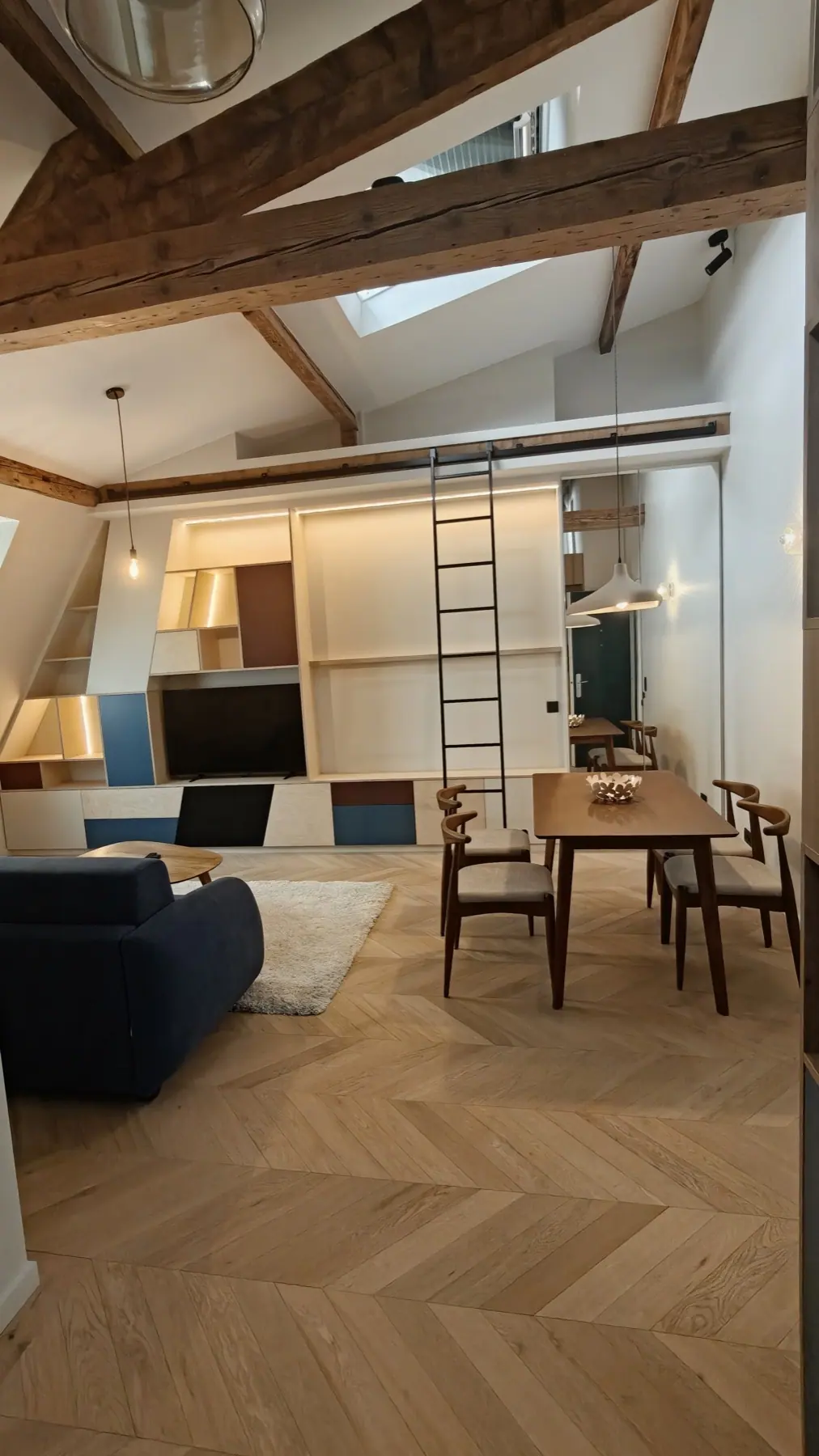 Séjour sous les combles avec poutres apparentes, bibliothèque sur mesure et parquet clair