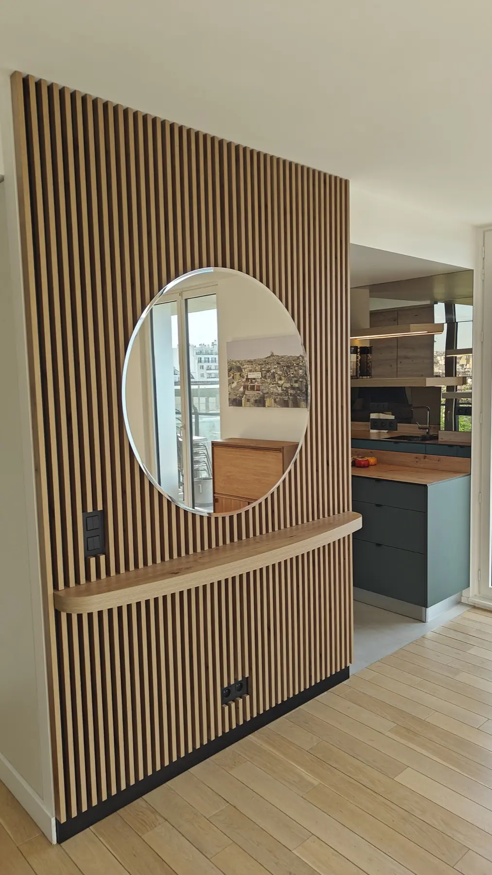 Cloison en tasseaux de bois avec miroir rond, ouverte sur la cuisine